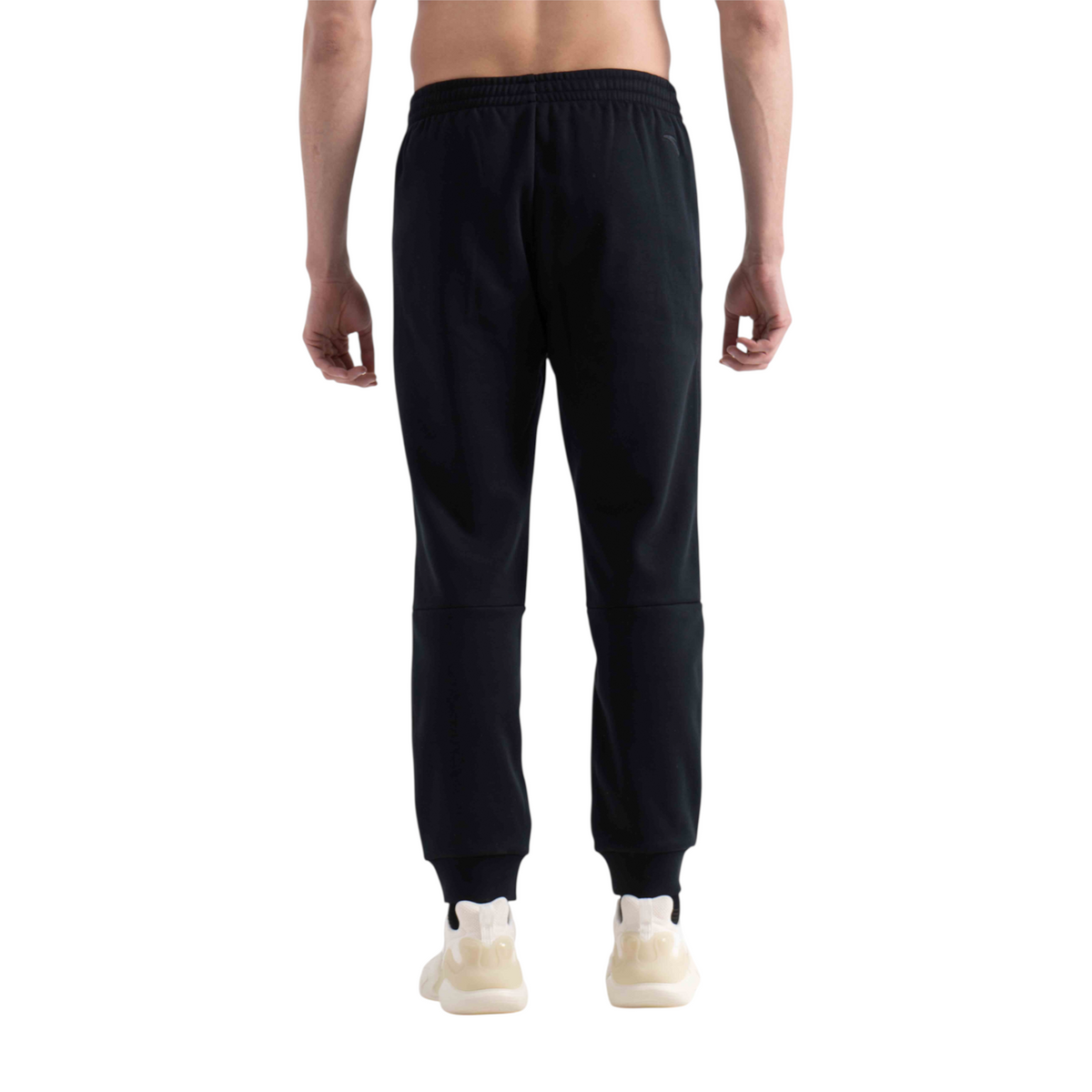 Back view of a man wearing FRG black knit track pants with elastic cuffs and a comfortable fit.