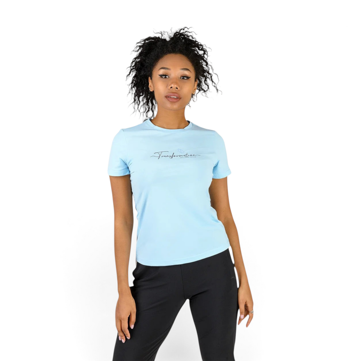 A woman wearing a light blue FRG cross training t-shirt with Transformation script logo on a plain background