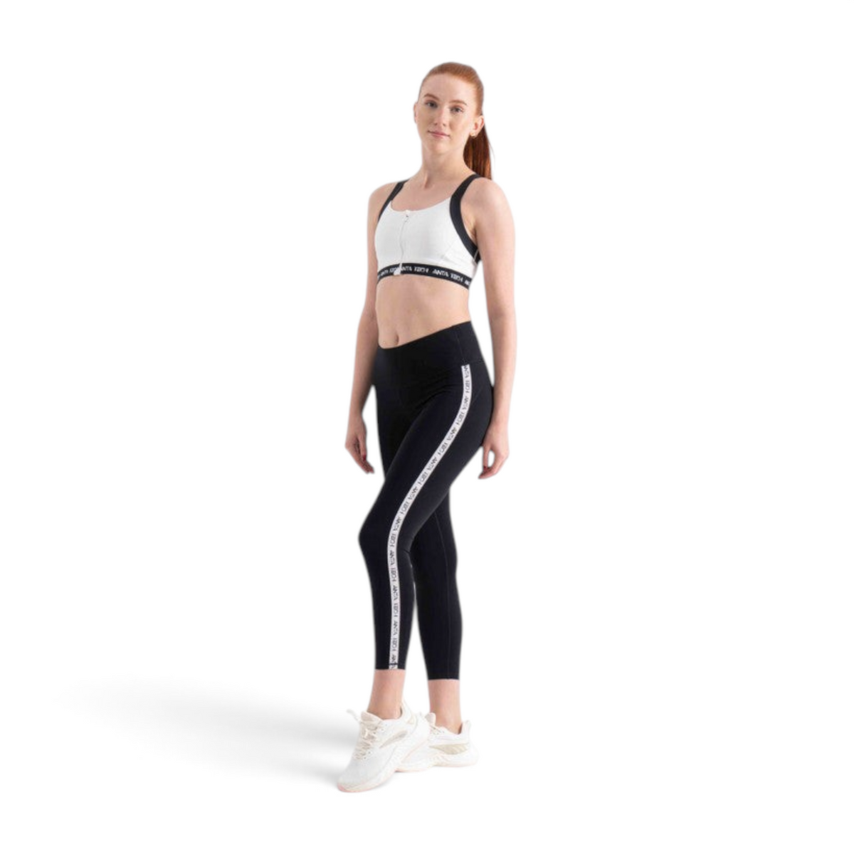 FRG model wearing a white sports bra and black leggings with branded side stripes and white athletic sneakers