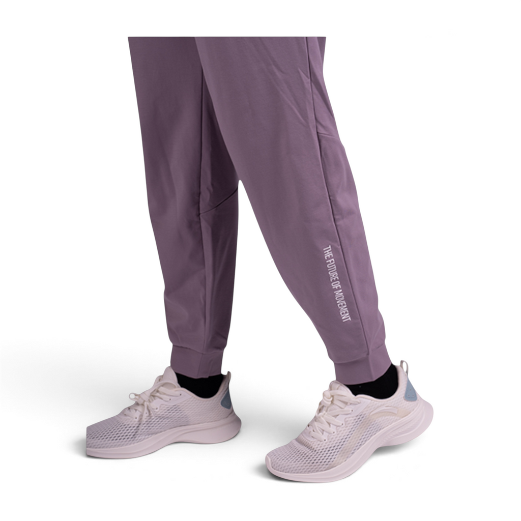 FRG knit ankle pants in dusty purple featuring a cuffed hem and white text detail, worn with white athletic sneakers.